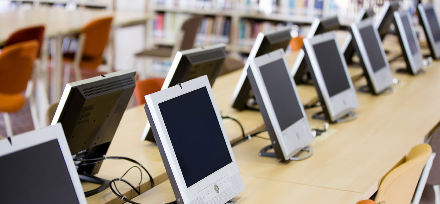 Row of computer monitors on a long desk in the library.!''